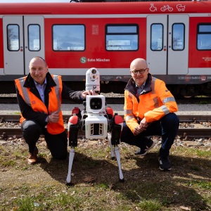 Zwei Bahnmitarbieter in Warnwesten mit Spot, dem Roboterhund