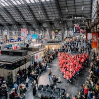 Luftaufnahme: viele Menschen am Bahnhof bilden ein Herz