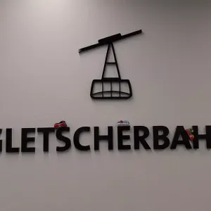 3 Spielfiguren fahren auf dreidimensionalen Buchstaben des Schriftzugs Gletscherbahn.
