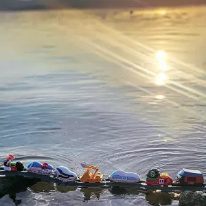 7 Spielfiguren stehen hintereinander auf einer schwimmenden Schiene im Wasser.