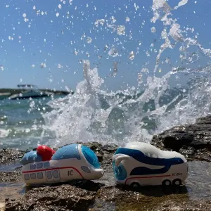Figuren Ida IC und der kleine ICE stehen in einer spritzenden Welle am Meer