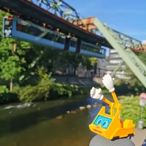 Figur Simsala SUM steht im Vordergrund, im Hintergrund fährt die Schwebebahn von Wuppertal.
