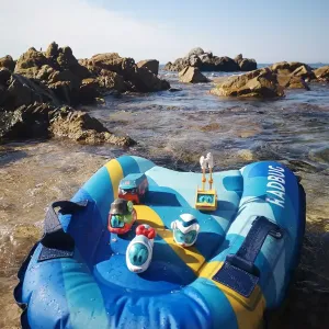 Diverse Spielfiguren stehen auf einer Luftmatratze am Strand.