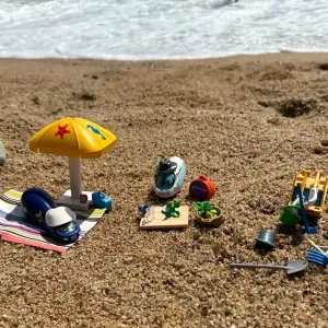 Verschiedene Spielfiguren stehen mit Buddelsachen am Strand.