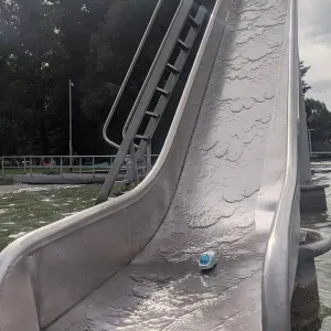 Figur der kleine ICE steht am Fuß einer Wasserrutsche im Nassen.