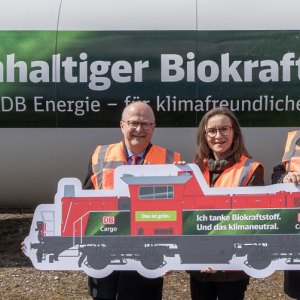 DB-Mitarbeitende vor einer Biokraft-Tankstellen mit LOK-Schild in der Hand