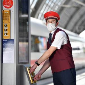 Bahnmitarbeitende mit roter Mütze am Zug