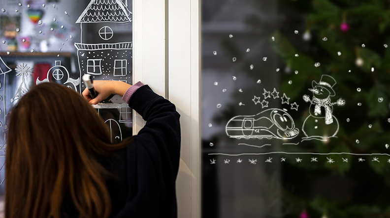 Ein Mädchen malt ein Bild am Fenster aus.