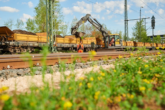 Ein Bagger arbeitet auf den Gleisen im Grünen