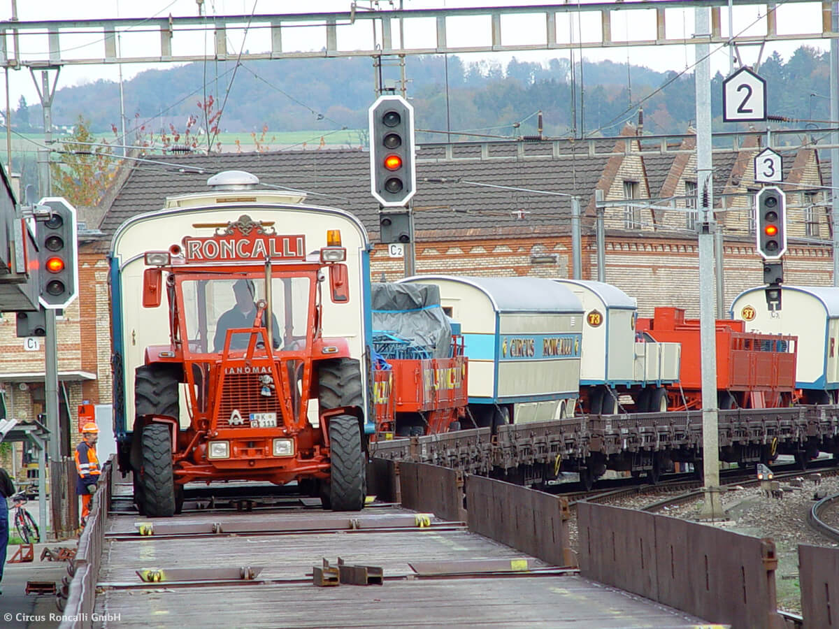 Ein roter Traktor zieht einen Roncalli-Wagen nach dem anderen auf die flachen Waggons