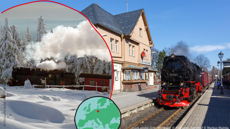 Eine schwarze Dampflok steht am Bahnhof. Im Winterbild fährt die Brockenbahn durch Schnee und Dampf.