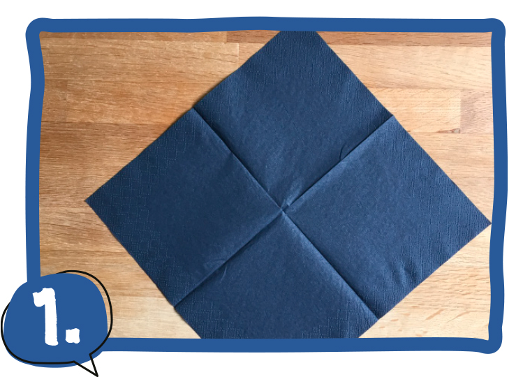 Eine dunkelblaue Serviette liegt aufgefaltet als Quadrat mit der Ecke nach oben auf einem Holztisch. Schritt 1 der Bastelanleitung.