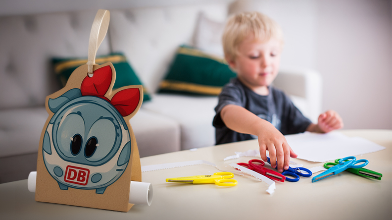 Kind bastelt mit Scheren; im Vordergrund steht eine Geschenktüte mit Comicfigur Ida IC