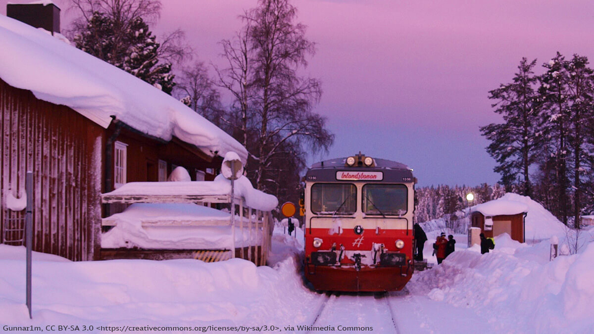 Schwedens Inlandsbanan Zug fährt auf einer verschneiten Strecke neben einem Bahnhof