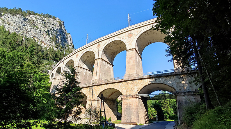 Steinbrücke mit mehreren großen Bögen zwischen Felsen und Bäumen.