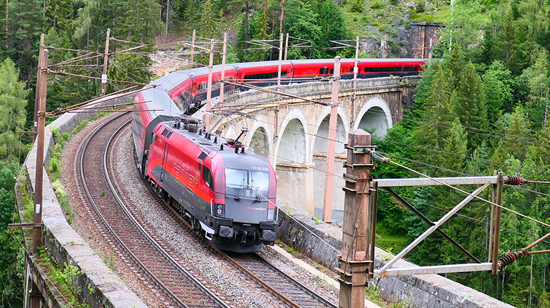 Roter Zug fährt über eine Brücke durch den Wald.