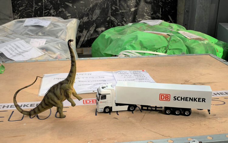Figur eines Dinosauriers neben einem Miniatur Bus auf einer Kiste