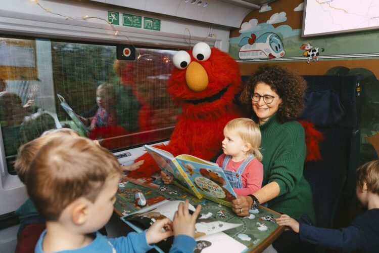 Im Kinderabteil wird Kindern am Tisch vorgelesen und auf einen der Plätze sitzt ein Charakter von der Sesamstraße zu sehen.