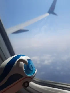 Figur Benni IC Bus guckt aus dem Fenster eines Flugzeugs auf Wolken.