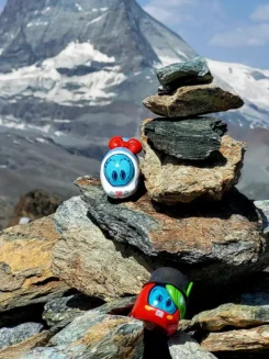 Spielfiguren Ida IC und Sally S-Bahn stehen auf einem Steinstapel im Hochgebirge