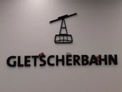 3 Spielfiguren fahren auf dreidimensionalen Buchstaben des Schriftzugs Gletscherbahn.