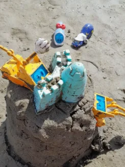 Verschiedene Spielfiguren bauen gemeinsam eine Sandburg am Strand.
