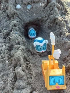 Verschiedene Spielfiguren kommen aus dem Tunnel einer Sandburg.