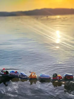 7 Spielfiguren stehen hintereinander auf einer schwimmenden Schiene im Wasser.