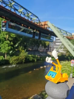 Figur Simsala SUM steht im Vordergrund, im Hintergrund fährt die Schwebebahn von Wuppertal.