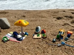 Verschiedene Spielfiguren stehen mit Buddelsachen am Strand.