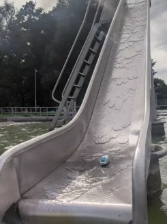 Figur der kleine ICE steht am Fuß einer Wasserrutsche im Nassen.
