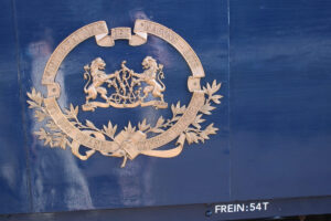 Das Logo der Compagnie Internationale des Wagons-Lits (CIWL) auf einem blauen Zugwaggon. Goldenes Emblem mit Schrift und zwei Löwen auf dunkelblauer Fläche.