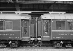Das Bild zeigt die Verbindung zwischen zwei Schlafwagen. Schlafwagen, auch bekannt als "Wagon-lit" (WL), sind Reisezugwagen, die Reisenden ermöglichen, liegend zu reisen. Schwarz-weiß Foto der Verbindung zwischen zwei alten Zugwaggons mit ovalen Türen.