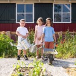 Der Garten in der Ausstellung Bahnwärtergärtlein wird von Kindern bewirtschaftet. © DB Museum/Daniel Karmann Drei Kinder mit Schubkarre im Garten des DB Museums