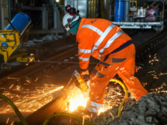 Gleisarbeiter in orangener Schutzkleidung beim schweißen an einer Weiche