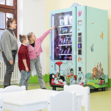 Verkaufsautomat im DB Museum mit Spielzeug; zwei Kinder zeigen auf Produkte, eine erwachsene Person steht daneben.