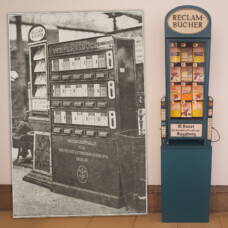 Historisches Foto eines Bücherautomaten neben einem modernen Nachbau „Reclam‑Bücher“ mit sichtbaren Heften.