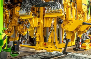 Detail einer Stopfmaschine mit gelbem Stopfaggregat und vielen Hydraulikleitungen über dem Gleis