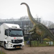 Auf den Hinterbeinen stehender Dinosaurier neben einem DB Schenker LKW