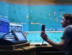 Ein Mann mit Telefon in der Hand sitzt an einem Schreibtisch vor mehreren Monitoren