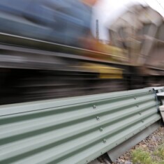 Schnellfahrender Güterzug fährt an einer Strecke mit niedriger Schallschutzmauer vorbei