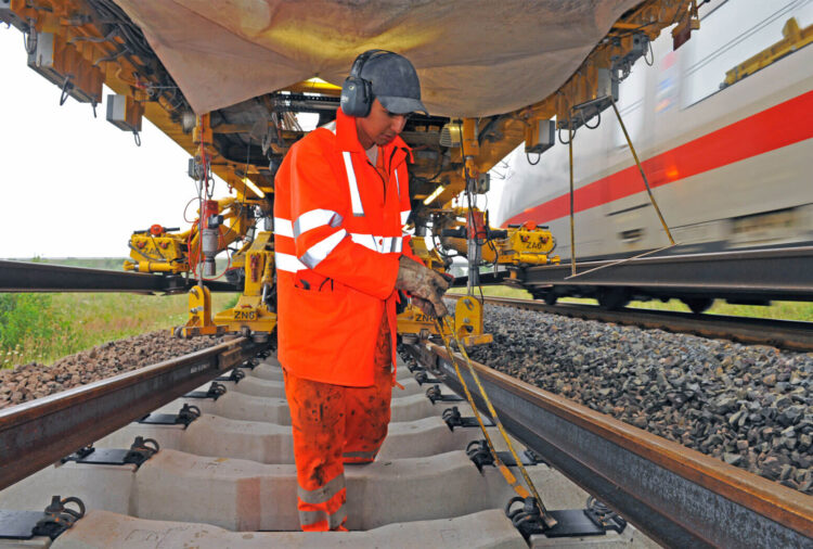 Ein Mitarbeiter der Bahn arbeitet an den Schwellen, während ein Zug an ihm vorbeifährt